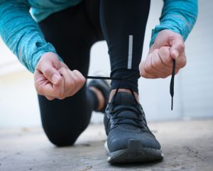 cropped image of someone kneeling down to tie the lace on their running shoe: image showing how gait analysis can benefit runners in Helensburgh
