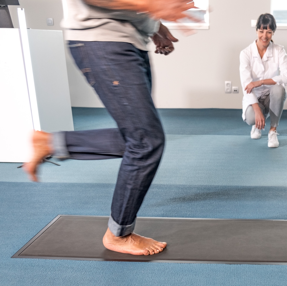 man wearing jeans and in bare feet running on footscan pressure mat for gait analysis while female physiotherapist in white coat looks on.