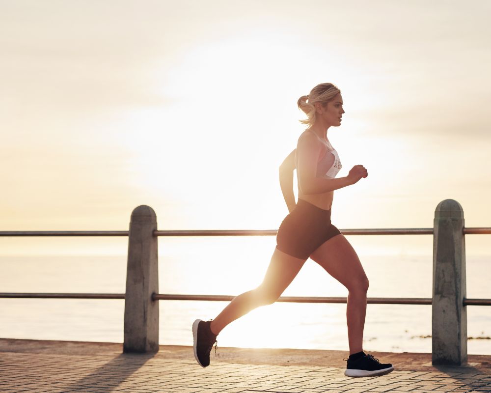 Female runner wearing shorts and a race number against a backdrop of water and sunshine.