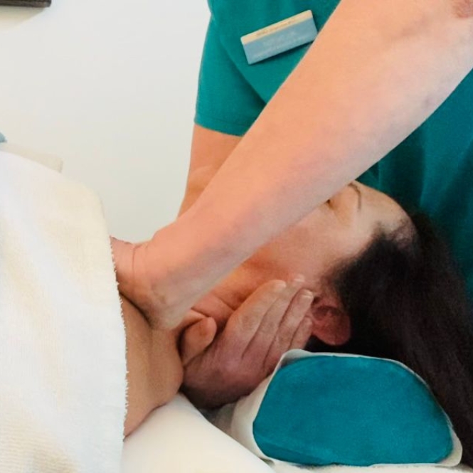 Woman lying on her back on a treatemrnt bed receives a head and neck massage from one of the integrated whole-person healthcare team at The Lomond Clinic