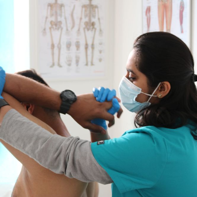 Physiotherapist Sakshi Duseja, part of the integrated whole-person healthcare team at The Lomond Clinic, examines a male patients arm and shoulder in a treatment room