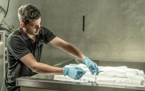Phits custom orthoses being made: man wearing blue gloves and a short sleevd black shirt removes components from tray of 3D printing composite powder