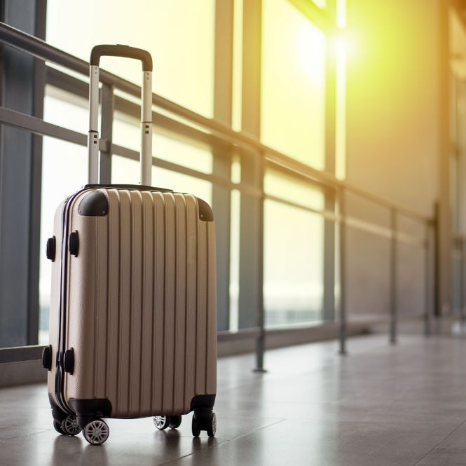 Wheeled suitcase on airport concourse with sun in background